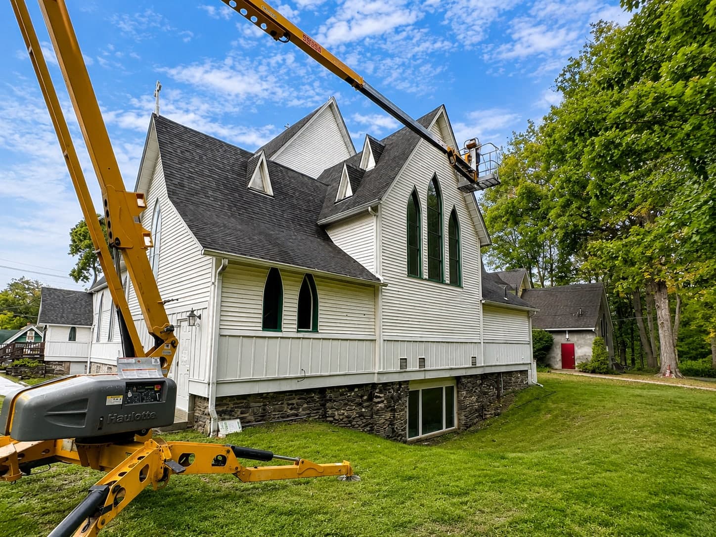 Boom lift working the gable end of a historic church with gothic windows during repainting