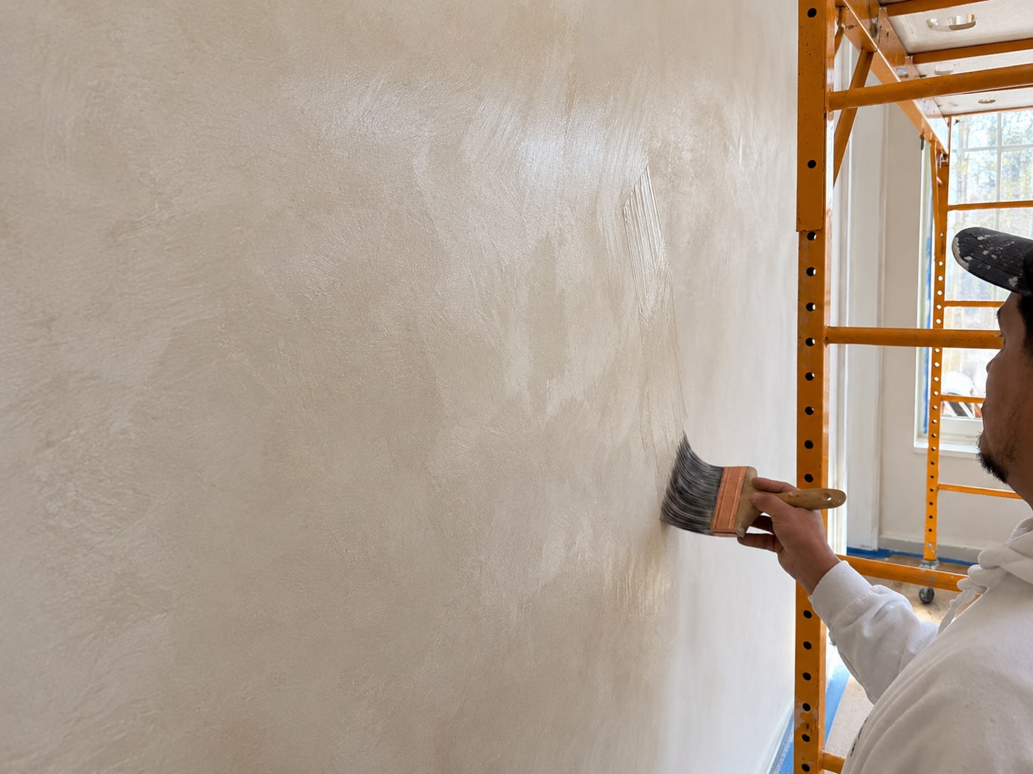 Painter laying a smooth skim coat across a prepared interior wall with a trowel